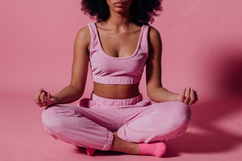 eine Frau in einem rosa farbenen Yoga Dress sitzt im Schneidersitz auf dem Boden und meditiert