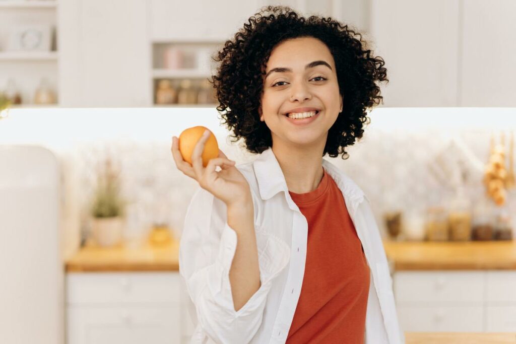 Eine Frau hält eine Orange in der Hand und freut sich darauf diese zu verspeisen