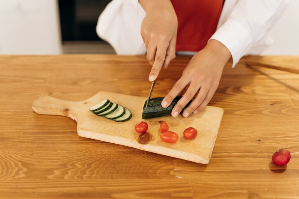 Eine Frau schneidet eine Gurke und Tomaten auf einem Holzbrett